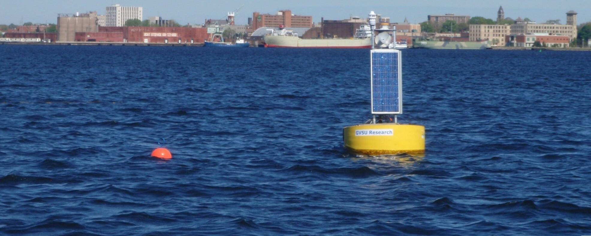 The Muskegon Lake Observatory buoy seen from the lake with downtown Muskegon visible on the horizon.